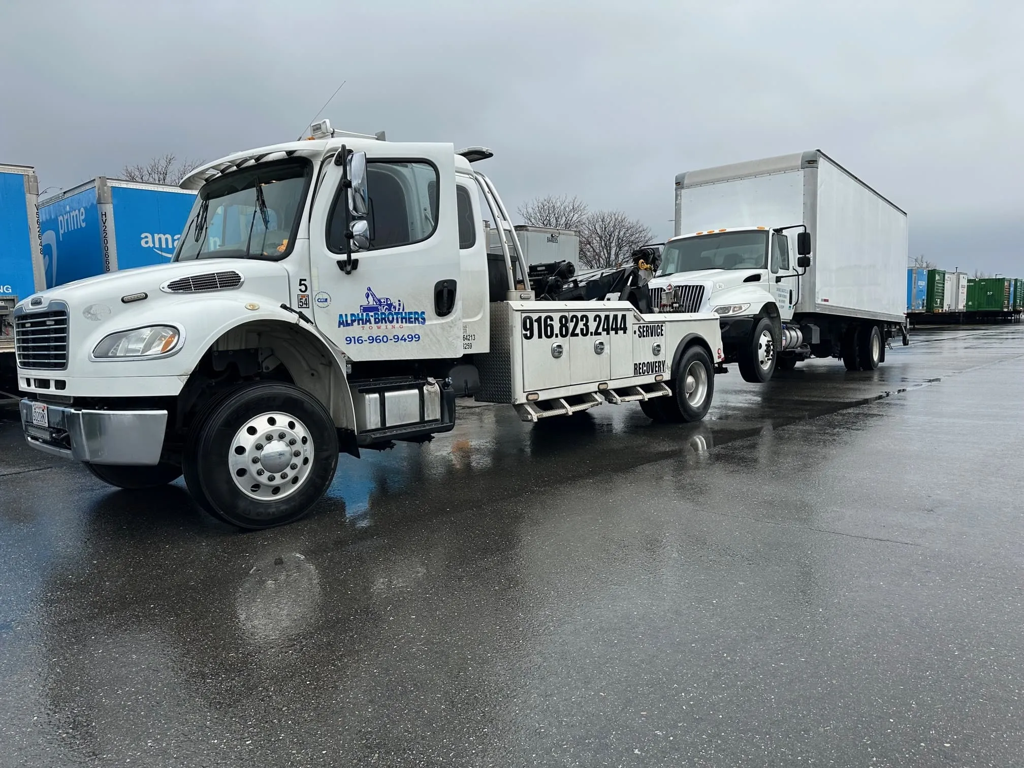 Alpha Brothers Freightliner medium-duty wrecker towing a commercial box truck in rainy Sacramento