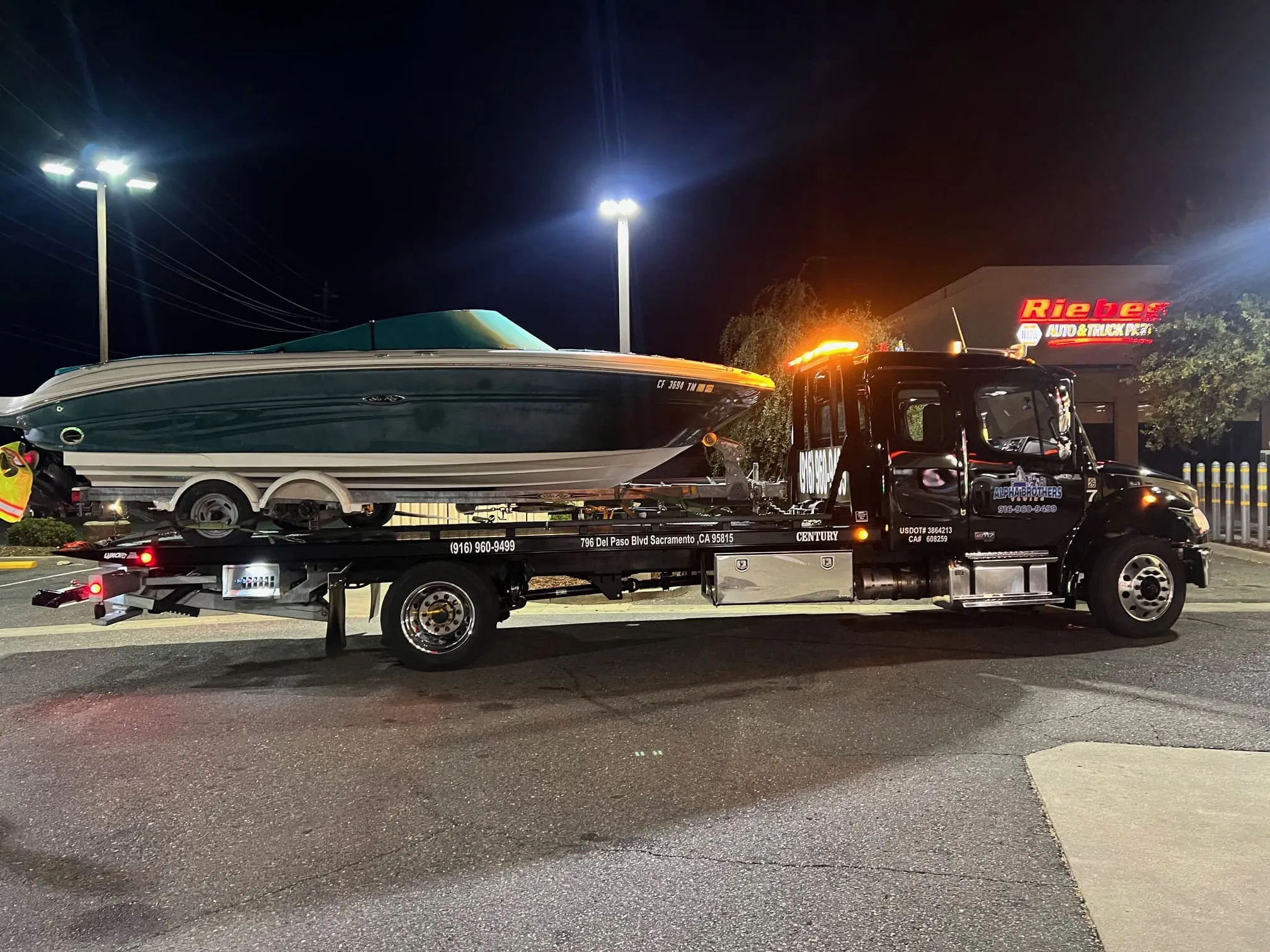 Alpha Brothers medium-duty flatbed tow truck hauling a speedboat at night in Sacramento