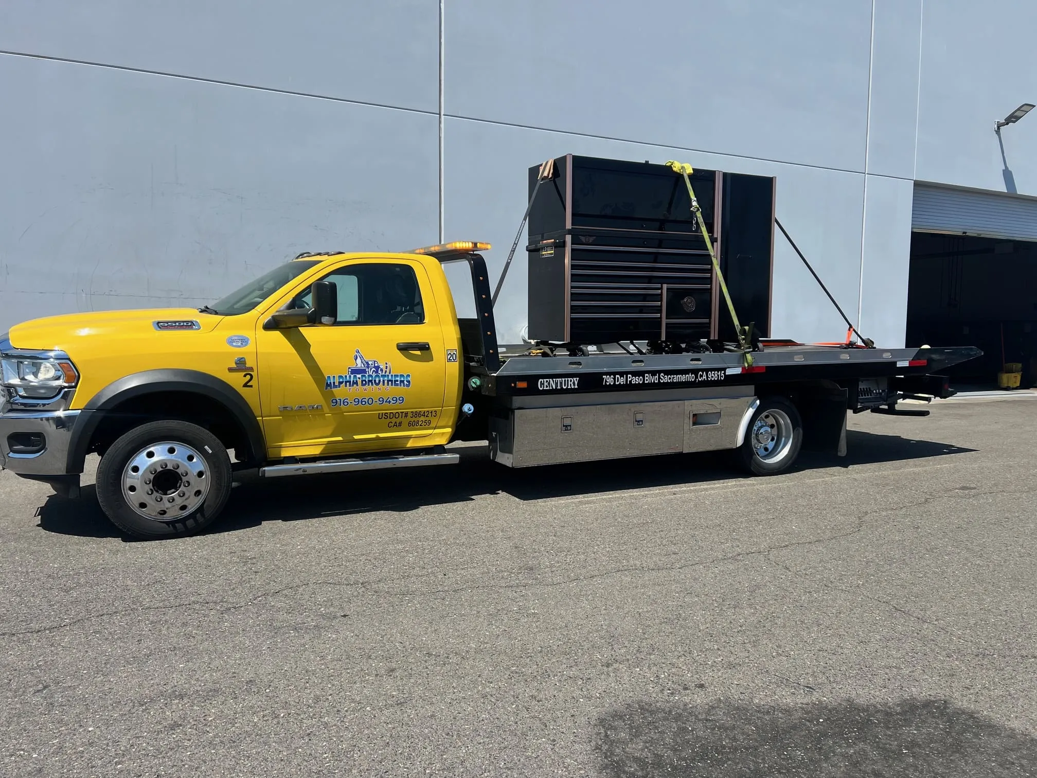 Alpha Brothers yellow Ram flatbed tow truck transporting a heavy tool cabinet at a Sacramento warehouse